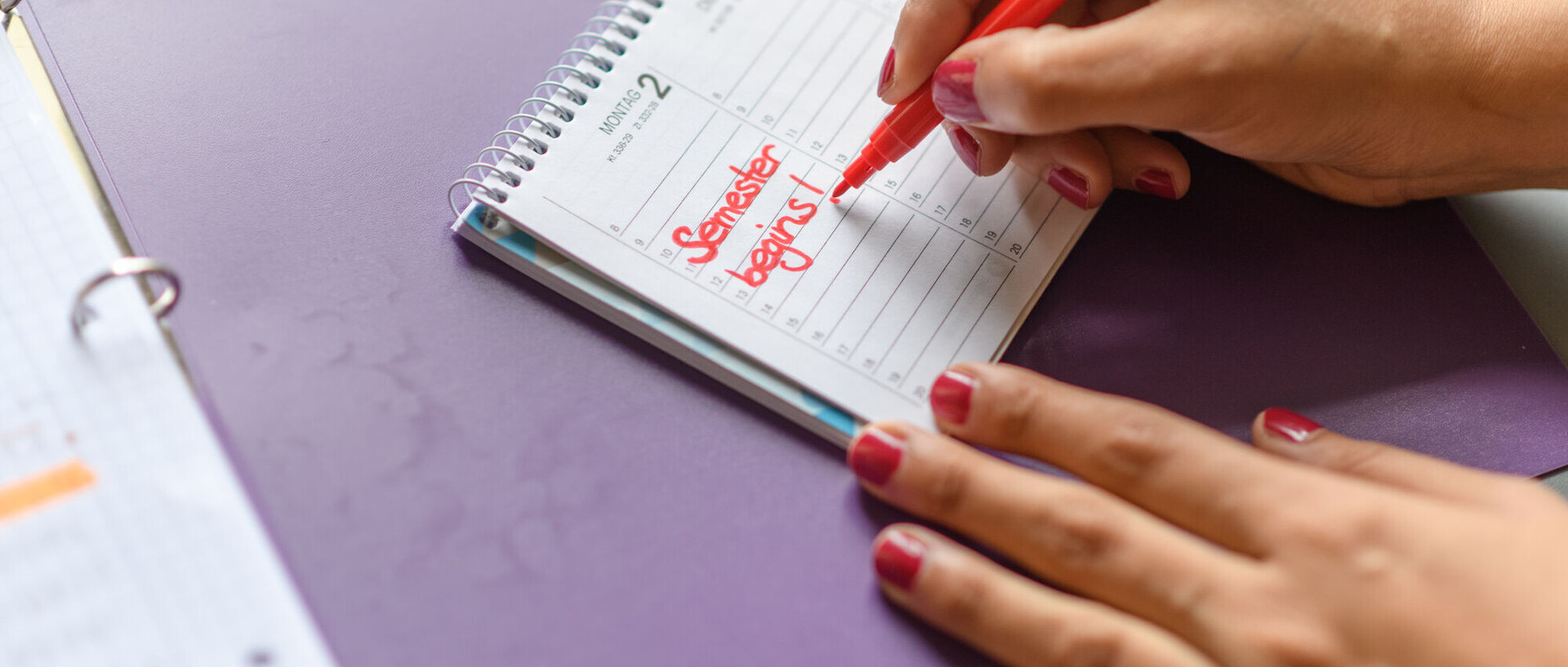 Eine Person schreibt mit Rotstift "Semester begins!" in einen Kalender.