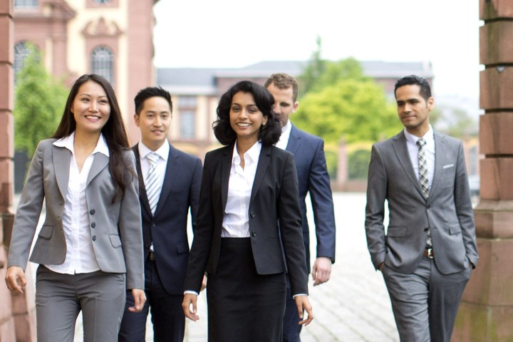 Studierende laufen in schicker Kleidung mit Anzügen, Blazern und Hemden über den Ehrenhof.