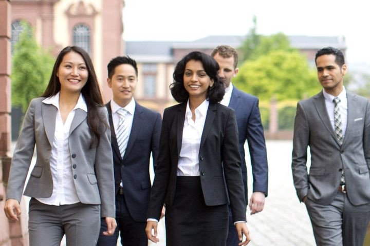 Studierende laufen in schicker Kleidung mit Anzügen, Blazern und Hemden über den Ehrenhof.