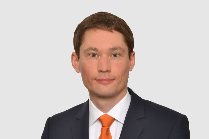 Prof. Bode hat kurze dunkle Haare und trägt ein weißes Hemd, ein dunkles Jacket und eine orangene Krawatte.