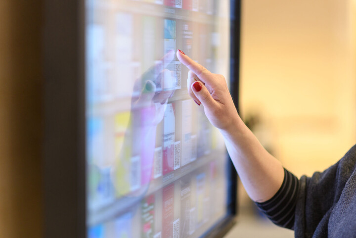 Eine Person bedient einen großen Touchscreen mit verschiedenen angezeigten Inhalten - nur Hand und Arm sind sichtbar.