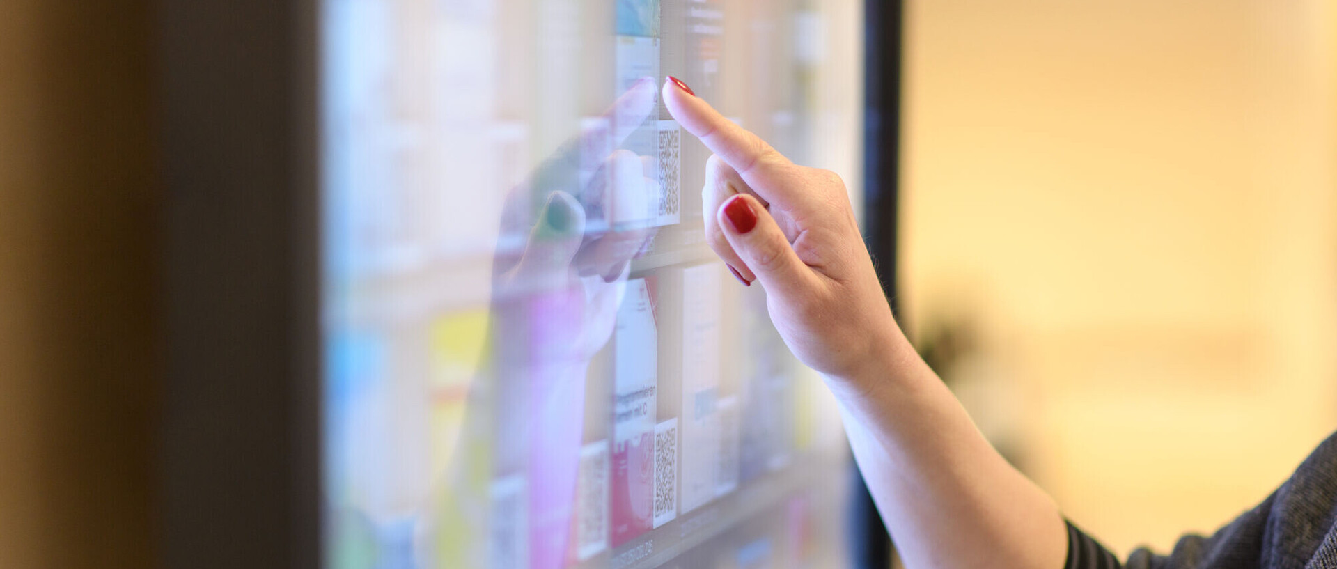 Eine Person bedient einen großen Touchscreen mit verschiedenen angezeigten Inhalten - nur Hand und Arm sind sichtbar.