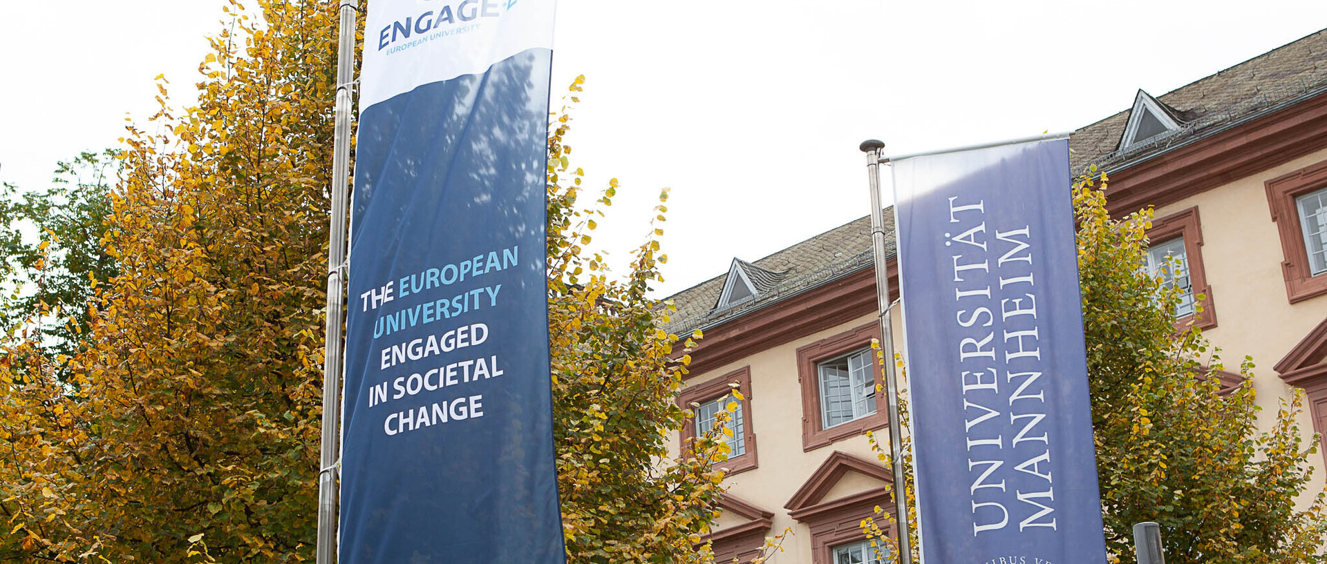 Eine Flagge von Engage.EU sowie eine Flagge der Uni Mannheim stehen vor dem Schloss der Uni.