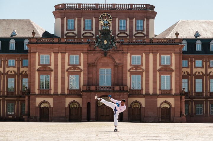 Vor dem Mannheimer Barockschloss kickt ein Mann in einer Karateuniform in die Luft.