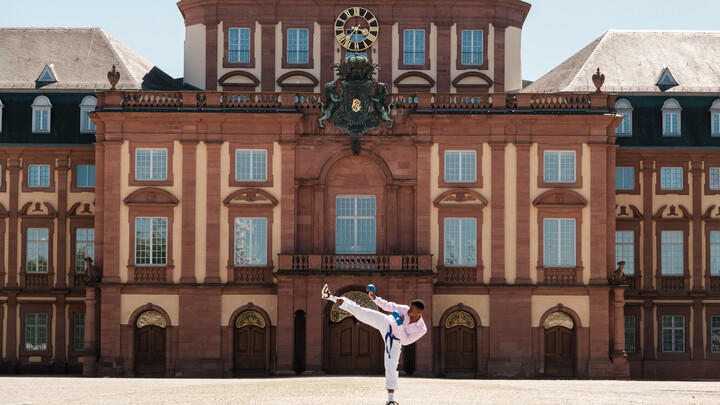 Vor dem Mannheimer Barockschloss kickt ein Mann in einer Karateuniform in die Luft.