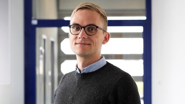 Ruben Bach trägt eine Brille, einen schwarzen Pullover und lächelt in die Kamera.