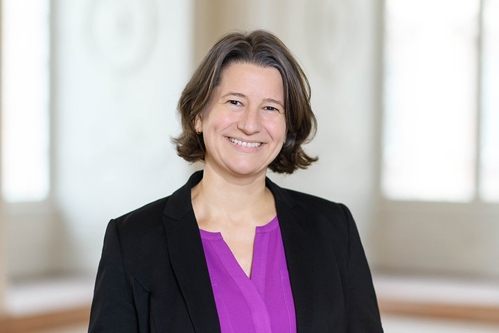 Dr. Katrin Schoppa-Bauer has brown medium-length hair. She is wearing a black blazer and a purple blouse.