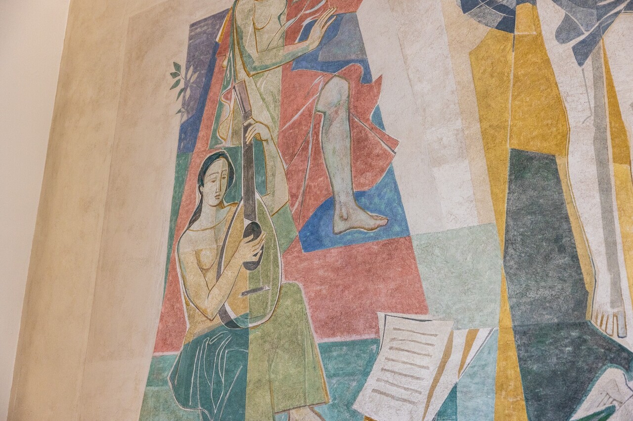 Ausschnitt einer bunten Wandmalerei: Eine Frau spielt sitzend auf einer Laute.