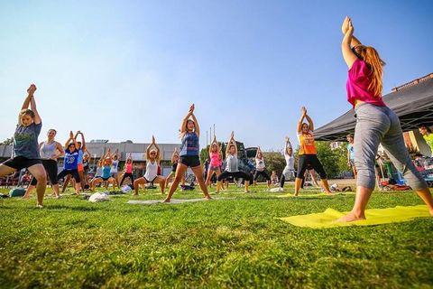 Junge Studentinnen machen auf einer grünen Wiese Yoga. Sie tragen bunte, sommerliche Sportbekleidung.