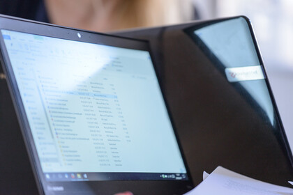 Ein Bildschirm, auf dem eine Dateiliste zu sehen ist, wird von der Sonne beschienen. Neben ihm befindet sich ein weiterer Laptop, der von hinten zu sehen ist.