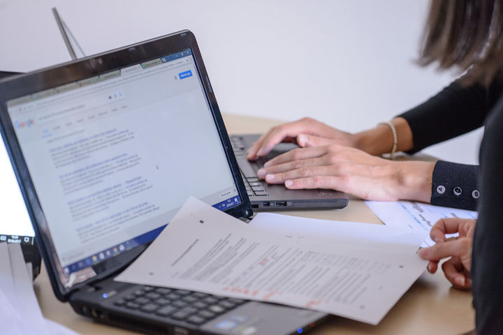 Zwei geöffnete Laptops auf einem Schreibtisch, Personen arbeiten mit Dokumenten.