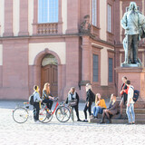 Eine Gruppe aus Studierenden versammelt sich um das Karl-Ludwig-Denkmal vor dem Schloss.