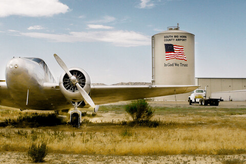 Im Vordergrund steht ein Flugzeug, dahinter ein Silo mit der USA-Flagge und der Aufschrift "South Big Horn County Airport, In God We Trust".