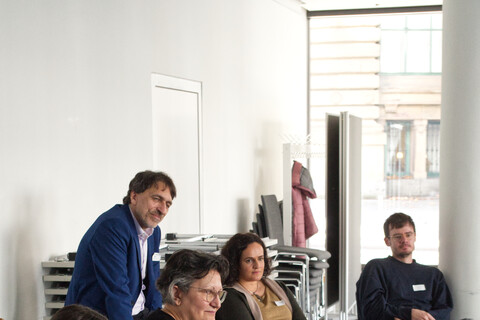 Workshopteilnehmende und -leitende diskutieren auf Stühlen und Tischen sitzend.