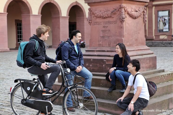 Vier Studierende sitzen lachend auf Stufen im Ehrenhof beisammen.