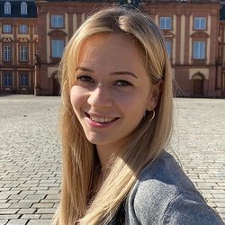 Alessa Bürkle hat lange, blonde Haare und lächelt. Sie trägt eine graue Strickjacke und ein schwarzes Top.