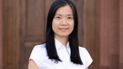 Chia-Yi Yen. She is wearing a white T-shirt and is standing in front of brown door.