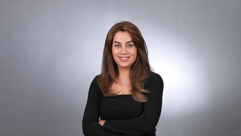 Nasim Karimi. She is wearing a black sweater and is standing in front of a grey photowall.