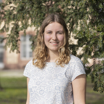 Laura Schmitt. Laura Schmitt trägt eine weiße Bluse und lächelt.