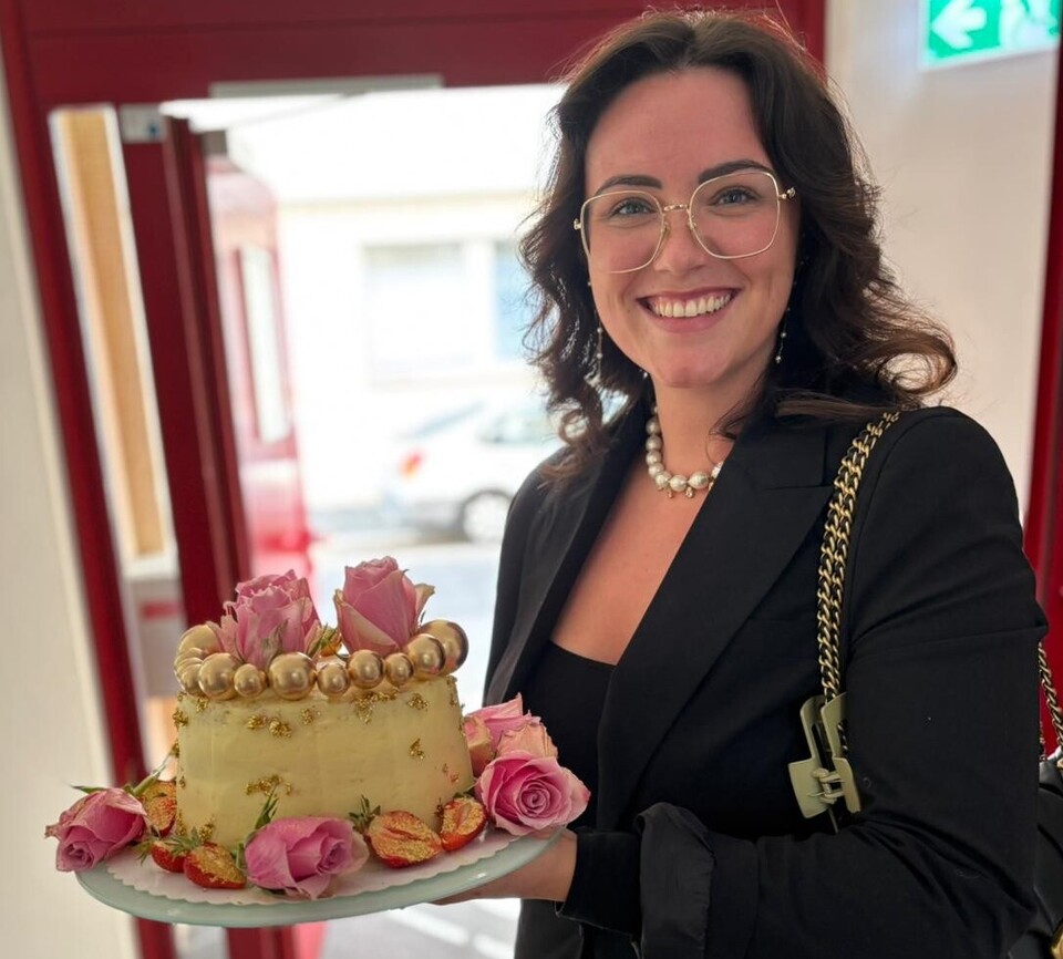 Studierende hält lächeln eine Torte in der Hand und zeigt sie der Kamera.
