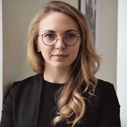 Sophie Horneber hat blonde lange Haare und eine runde, schwarzumrandete Brille. Sie trägt ein schwarzes geripptes Oberteil und daüber einen schwarzen Blazer.