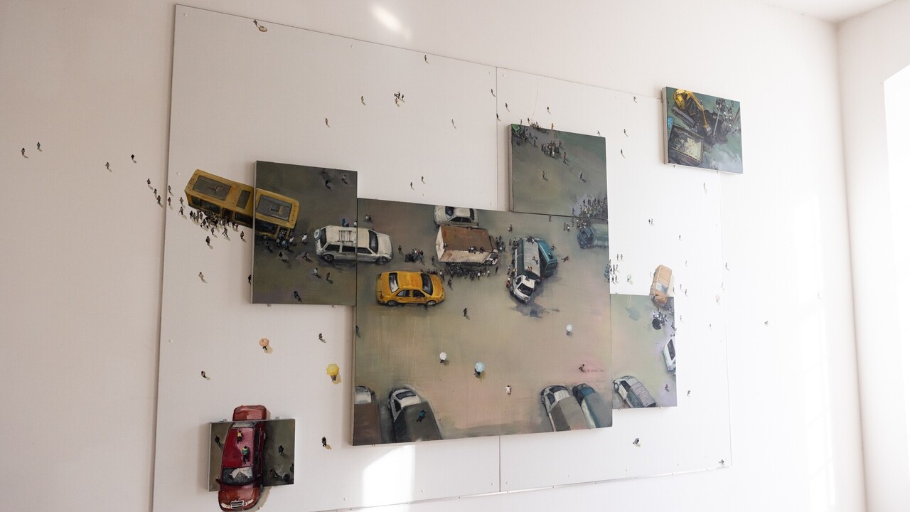 Gemälde einer Person mit Miniaturfiguren, das sich auf die Wand fortsetzt. An einer Stelle sind Autos, Figuren und ein Verkehrschaos mit Unfall dargestellt