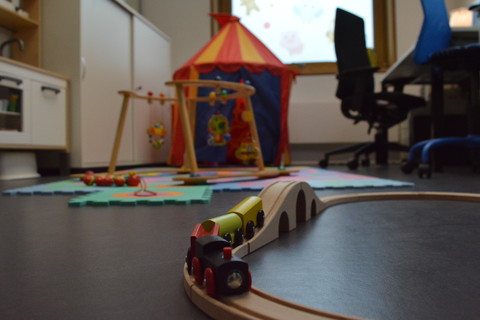 Eltern-Kinder-Zimmer der Universität Mannheim. Im Hintegrund Schreibtisch für Elternteil und Kind. Auf dem Boden liegen Spielsachen.