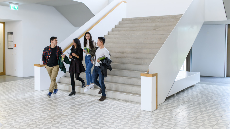 International Studierende B6_Anna Logue Vier Studierende laufen eine Treppe des B6-Bauteils der Uni Mannheim runter.