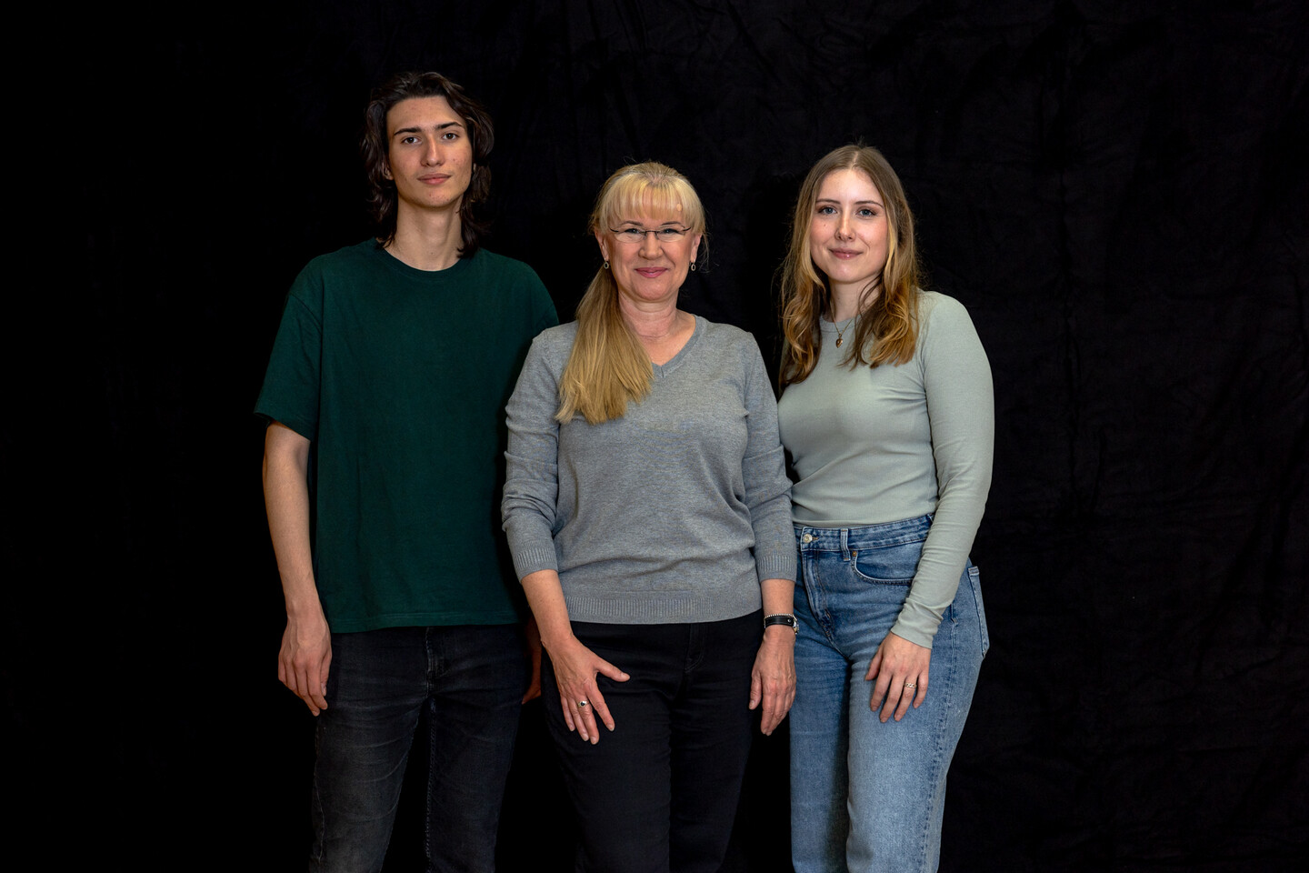 Drei Personen, zwei Frauen und ein Mann, stehen nebeneinander vor einem schwarzen Hintergrund.