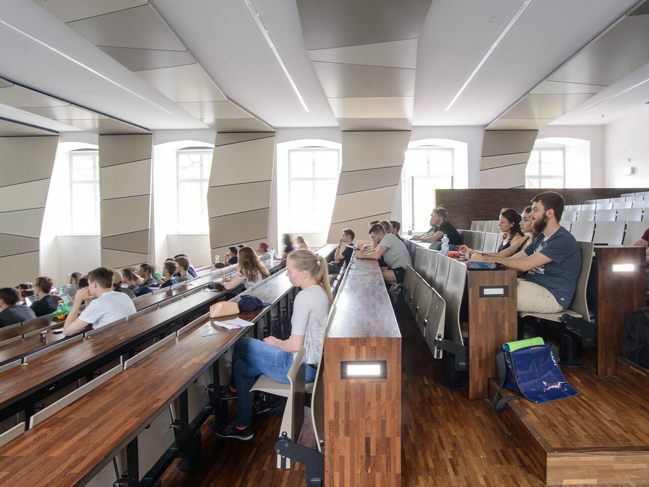 Lecture in Lecture Hall SO 108 Studierende in einem hölzernen, lichtdurchfluteten Hörsaal mit vielen Fenstern