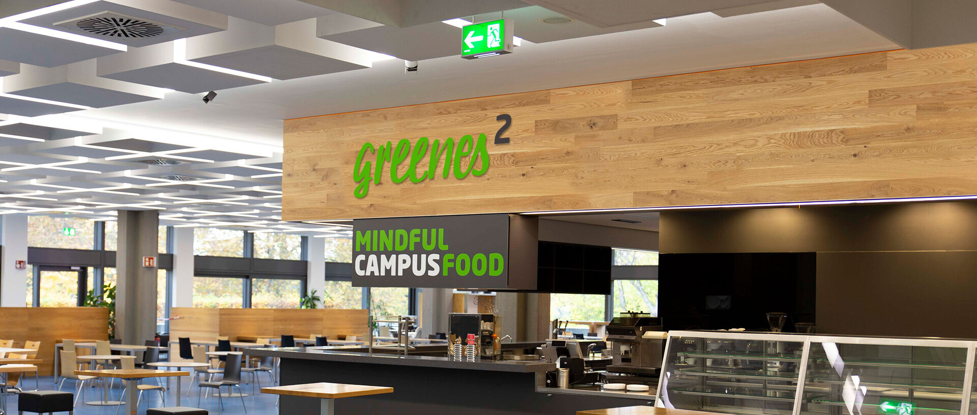 Ausschnitt der Mensaria der Uni Mannheim mit der Theke von greenes, dem Gastronomiekonzept, im Vordergrund. Auf einem Schild steht der Schriftzug "mindful campus food".  