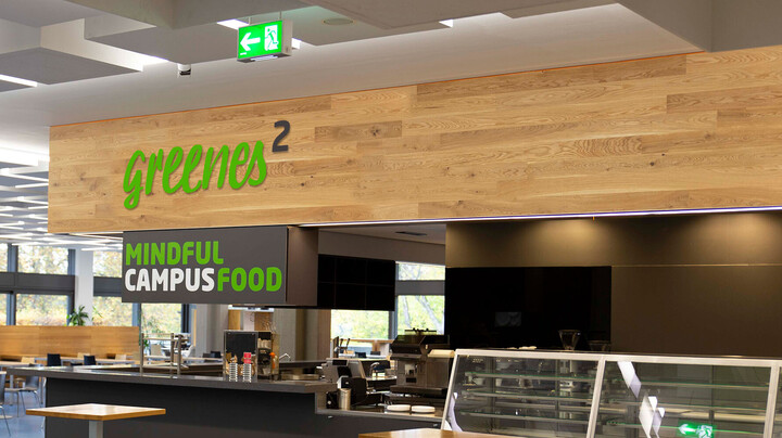 Ausschnitt der Mensaria der Uni Mannheim mit der Theke von greenes, dem Gastronomiekonzept, im Vordergrund. Auf einem Schild steht der Schriftzug "mindful campus food".