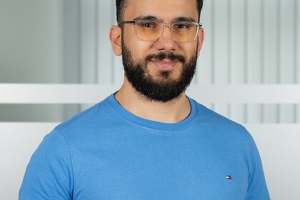 Porträt von Nader Hotait. Er hat kurze schwarze Haare, einen Bart und eine Brille. Er trägt ein blaues T-Shirt.