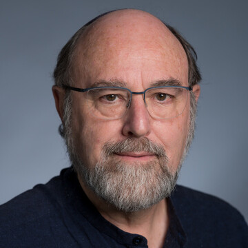 David Leiser hat kurze graue Haare und einen Bart. Er trägt eine Brille und ein schwarzes Hemd