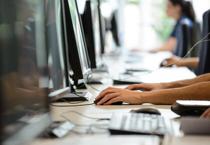 Vier Menschen sitzen in einer Reihe vor Computern.