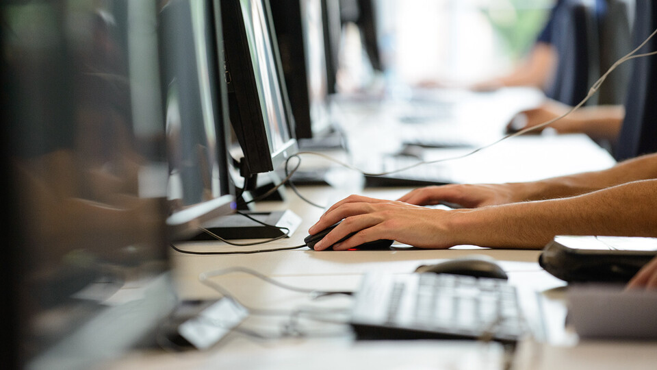 Vier Menschen sitzen in einer Reihe vor Computern.