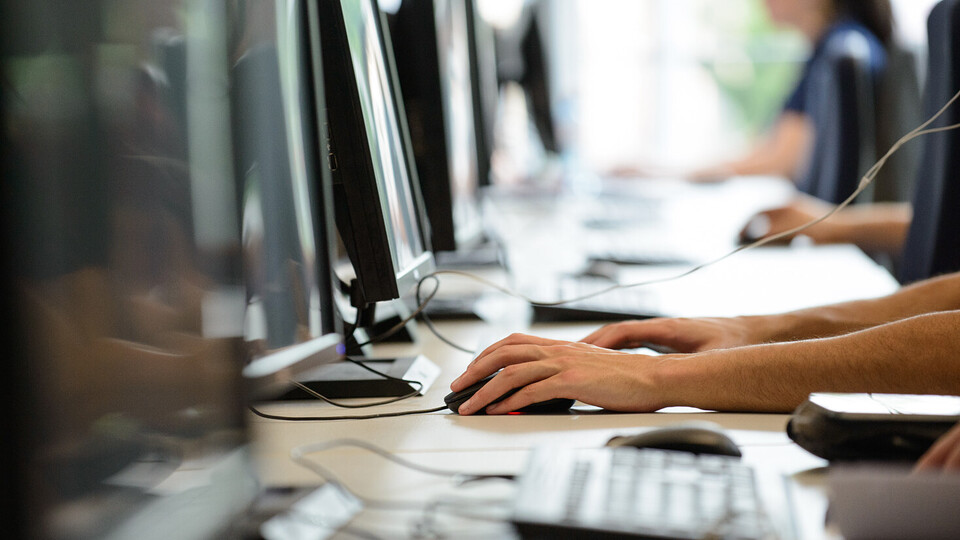 Vier Menschen sitzen in einer Reihe vor Computern.