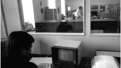 Eine schwarz-weiß Aufnahme des Rechenzentrums, auf der ein Mensch an einem Computer sitzt.