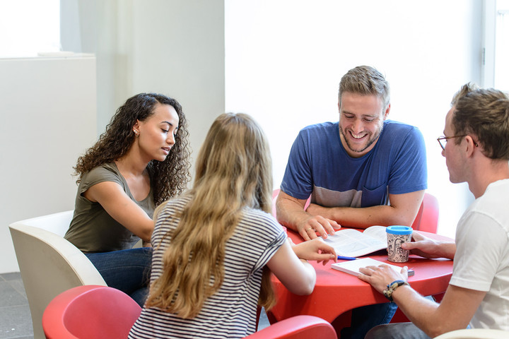 Vier Studierende sitzen an einem runden Tisch und lernen gemeinsam.