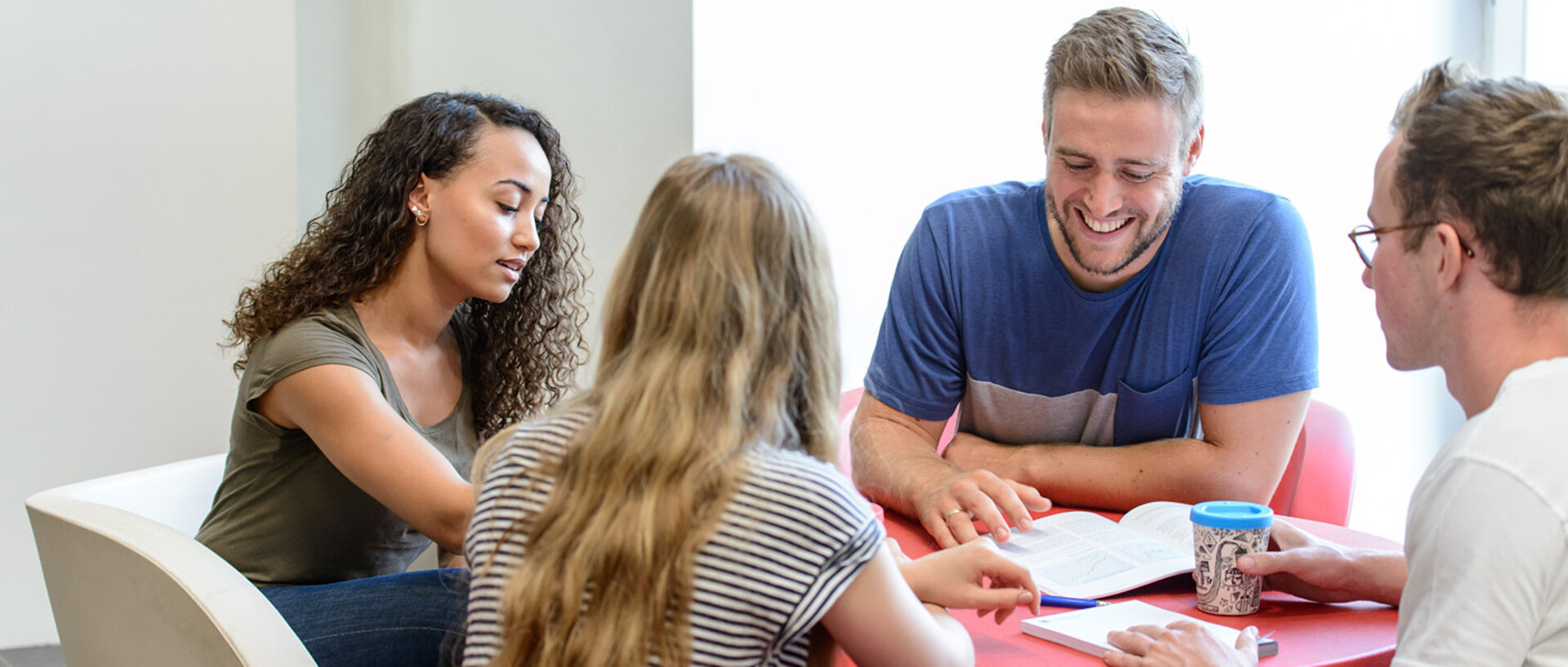 Vier Studierende sitzen an einem runden Tisch und lernen gemeinsam.