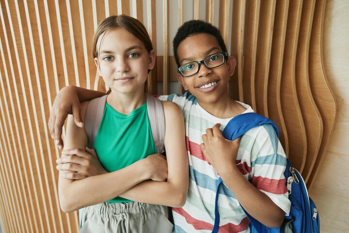 Zwei Kinder stehen vor einer Wand. Ein Kind hat den Arm um das andere Kind gelegt.