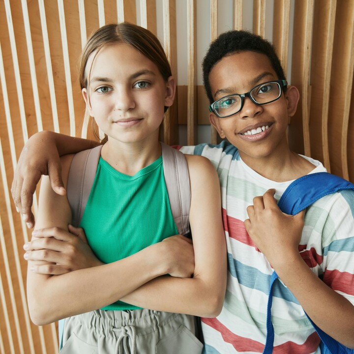 Zwei Kinder stehen vor einer Wand. Ein Kind hat den Arm um das andere Kind gelegt.