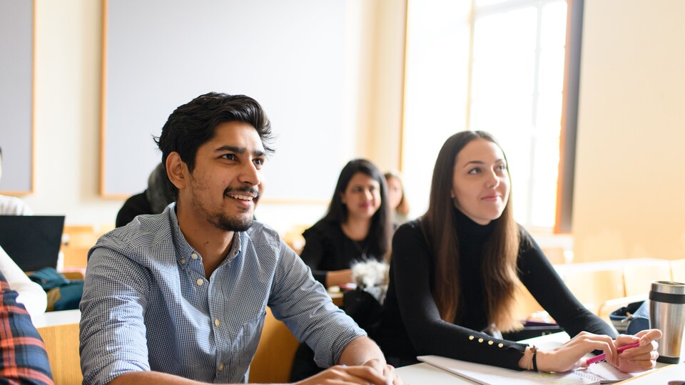In einem Seminarraum sitzen sechs Studierende, die erwartungsvoll nach vorn schauen