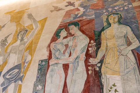 Ausschnitt eines Wandbildes: Ein Paar hält sich in den Armen. Links von ihnen hebt eine halbnackte Frau den Arm nach oben. Rechts steht eine weitere Frau mit einem Zweig in der Hand.