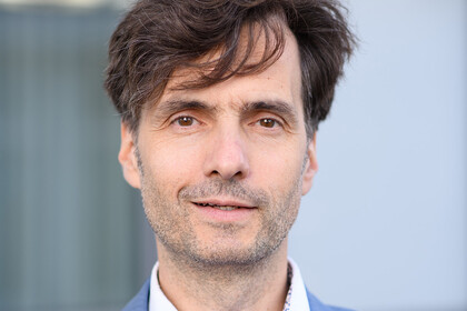 Portrait von Georg Alpers. Er trägt ein weißes Hemd sowie einen blauen Blazer und lächelt.