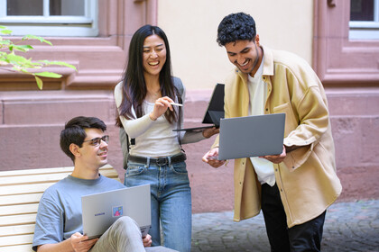 Drei Personen mit Laptops unterhalten sich lachend im Rektoratshof der Universität.