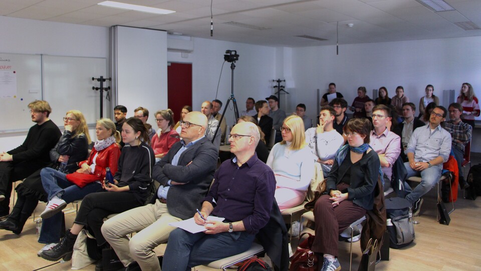 Die Teilnehmenden der Summer School sitzen in einem modernen Konferenzraum und hören aufmerksam zu.