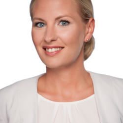 Portrait einer Frau mit hellblonden Haaren, welche sie in einem Dutt trägt, blauen Augen und einem schönen Lächeln. Sie trägt eine weiße Bluse mit einem weißen Blazer darüber.