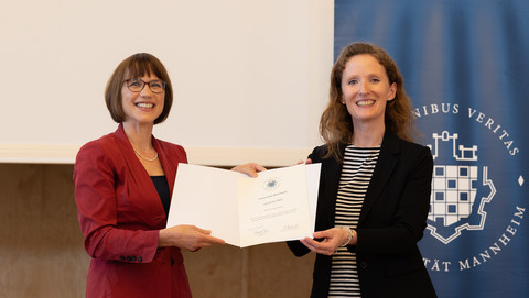 Zwei Personen in schicker Kleidung stehen auf einer Bühne. Beide halten eine Urkunde für einen Lehrpreis der Uni Mannheim in der Hand.