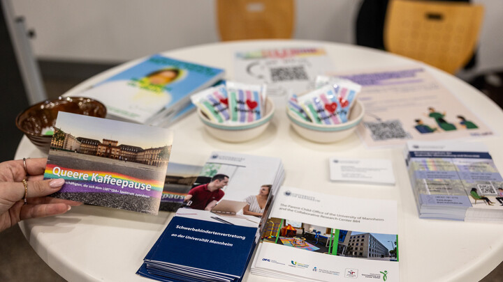 Im Stand an der Mensa zur Diversity Week 2025 steht ein Tisch mit mehreren Visitenlkarten, Postern und Gummibärchen.